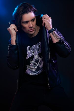 Moody portrait of person in dark hoodie with Slayer band shirt against black background.
