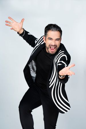 Energetic performer in black and white striped jacket poses expressively against light background.