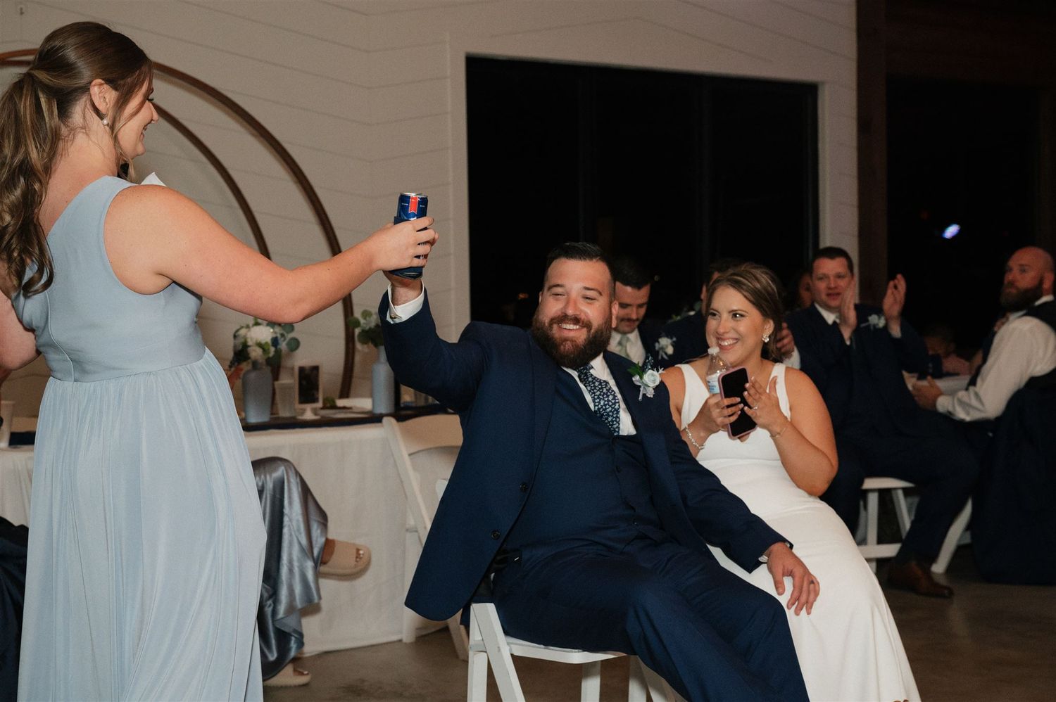 Wedding guests capture photos while the couple enjoys a seated moment at the reception.