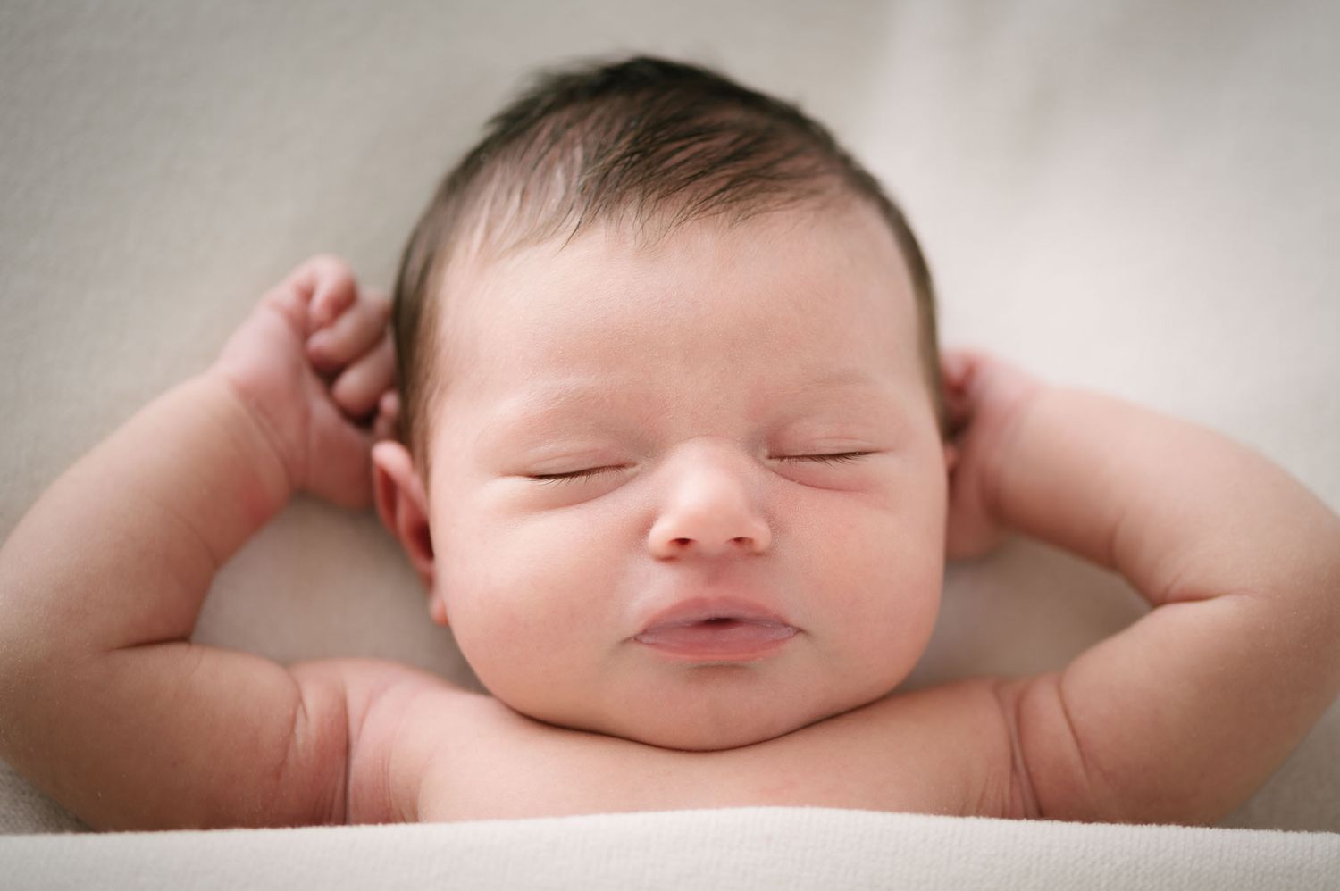 Close-up portrait of sleeping newborn baby with hands behind head.