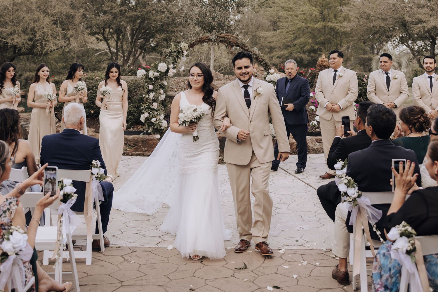 Newlyweds walk down the aisle while guests capture the moment on their phones.