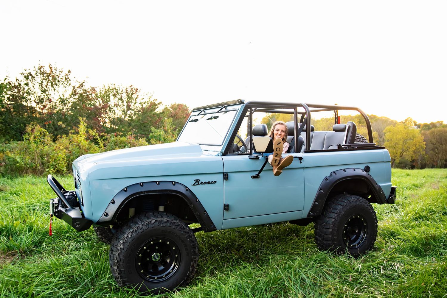 Light blue vintage Jeep displayed in grassy field during sunset.