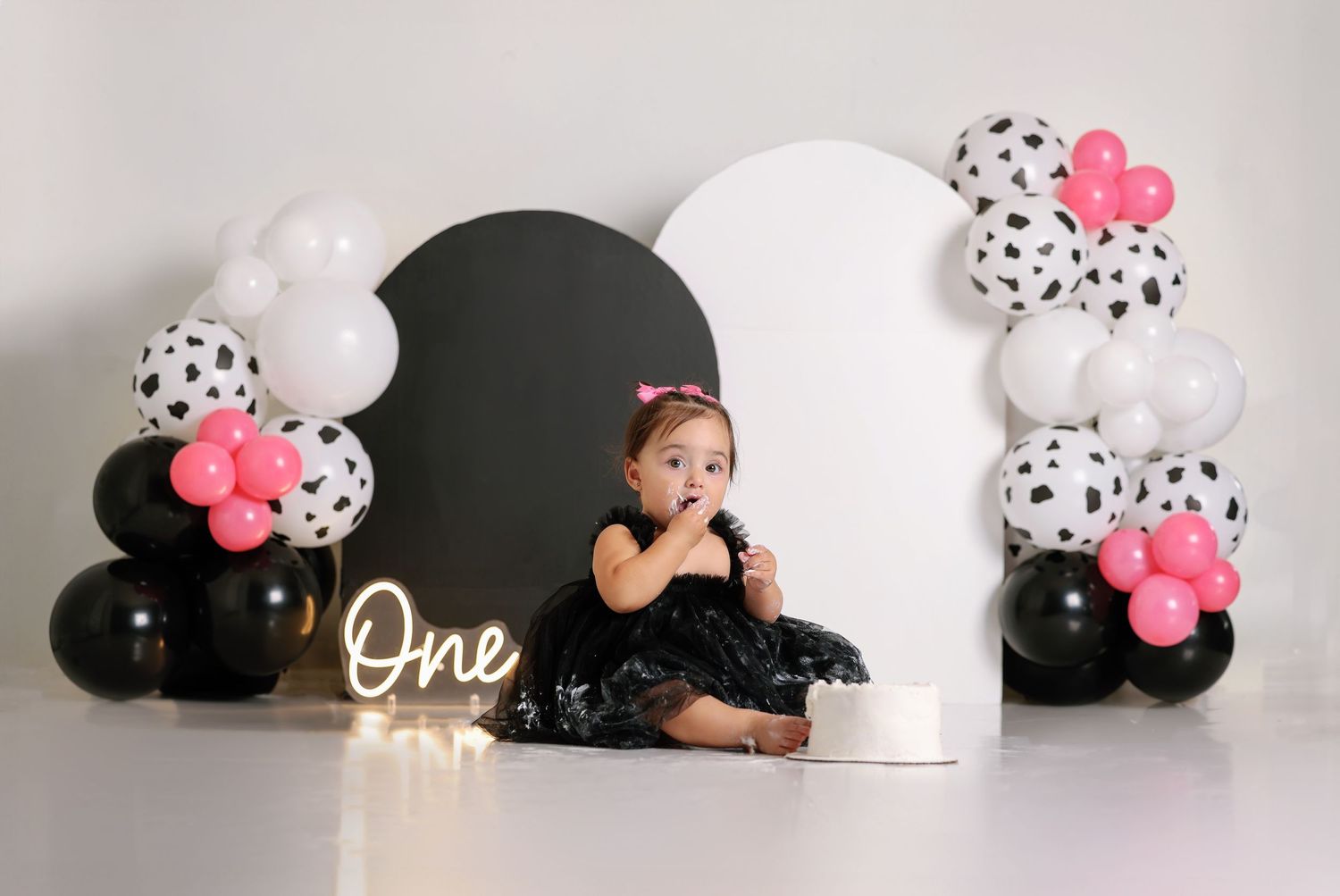 Black and white balloon arch with pink accents for first birthday celebration.
