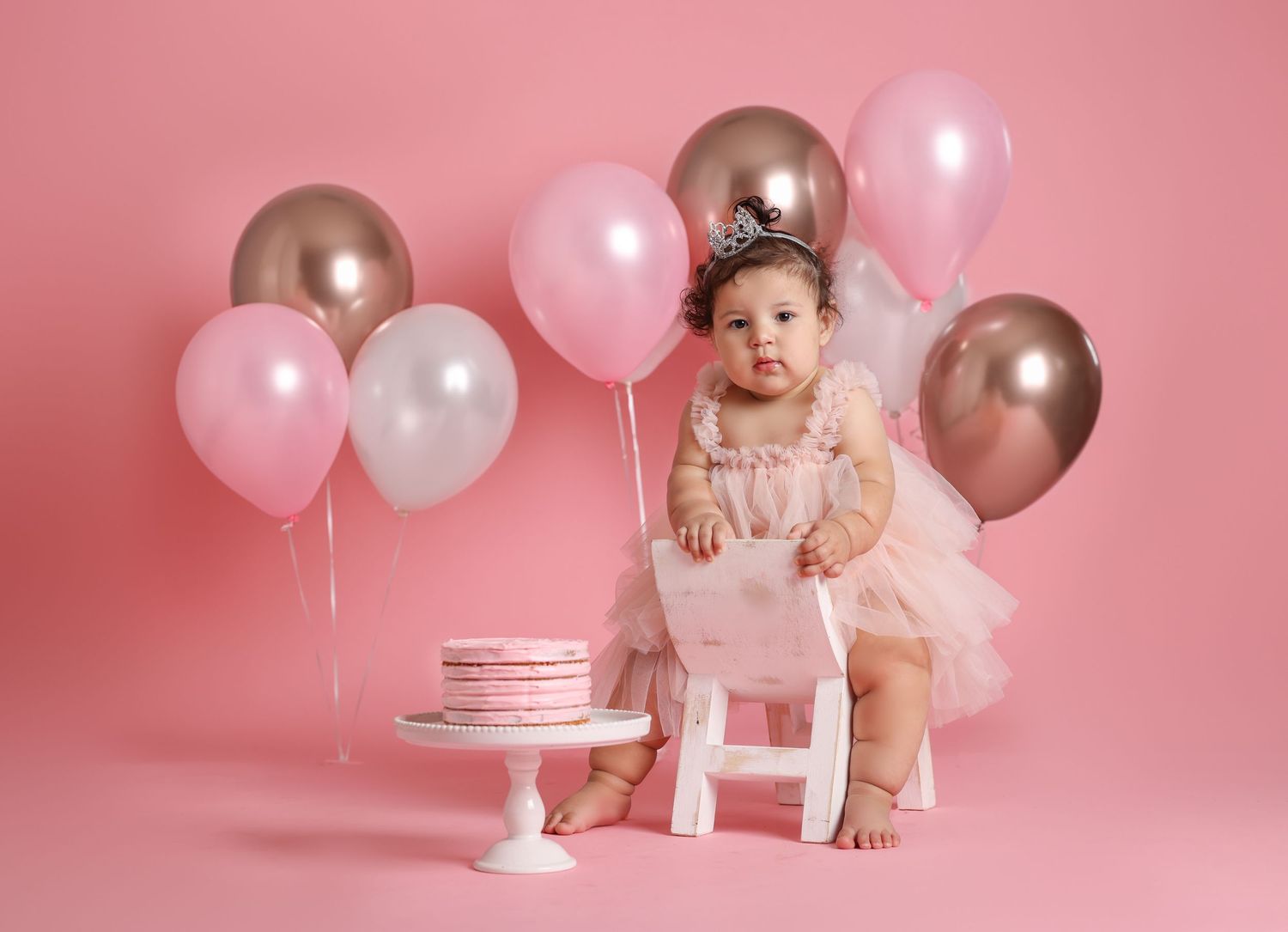 First birthday celebration setup with pink and gold balloons and small cake.