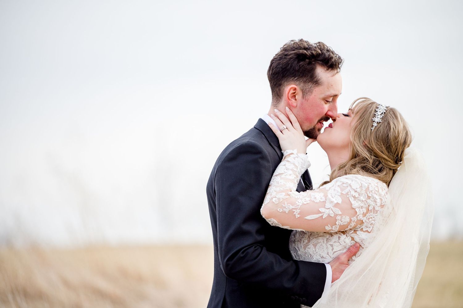 A romantic wedding couple shares a tender kiss in a field with soft lighting and a light colored background by Stephanie Coulter Photography