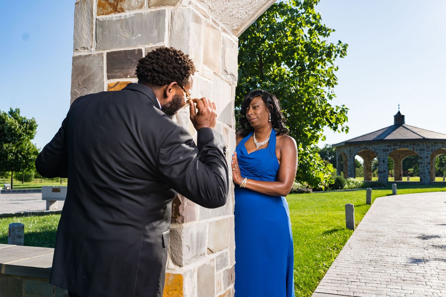 Couple shares intimate moment near stone pillar during outdoor proposal.