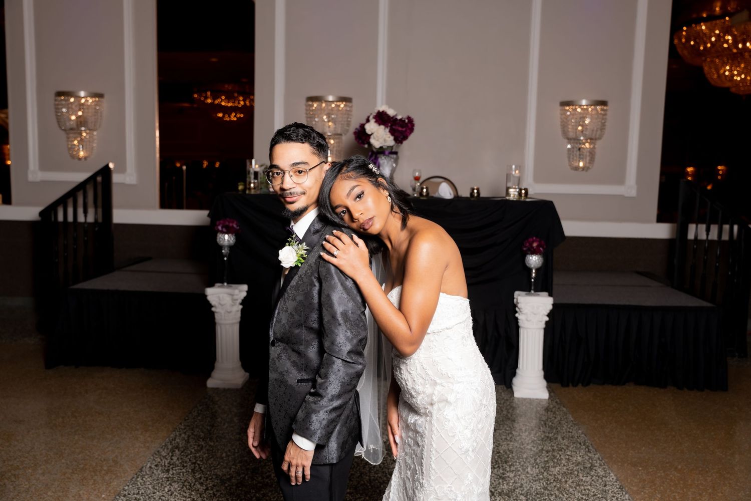Wedding couple shares playful moment in elegant ballroom with chandeliers.