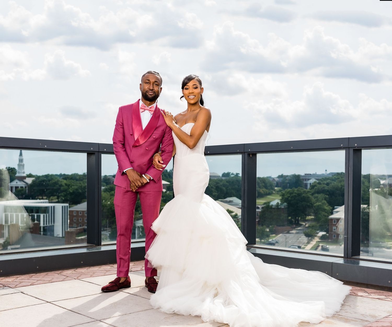 Wedding couple poses on rooftop terrace with pink suit and flowing white gown.