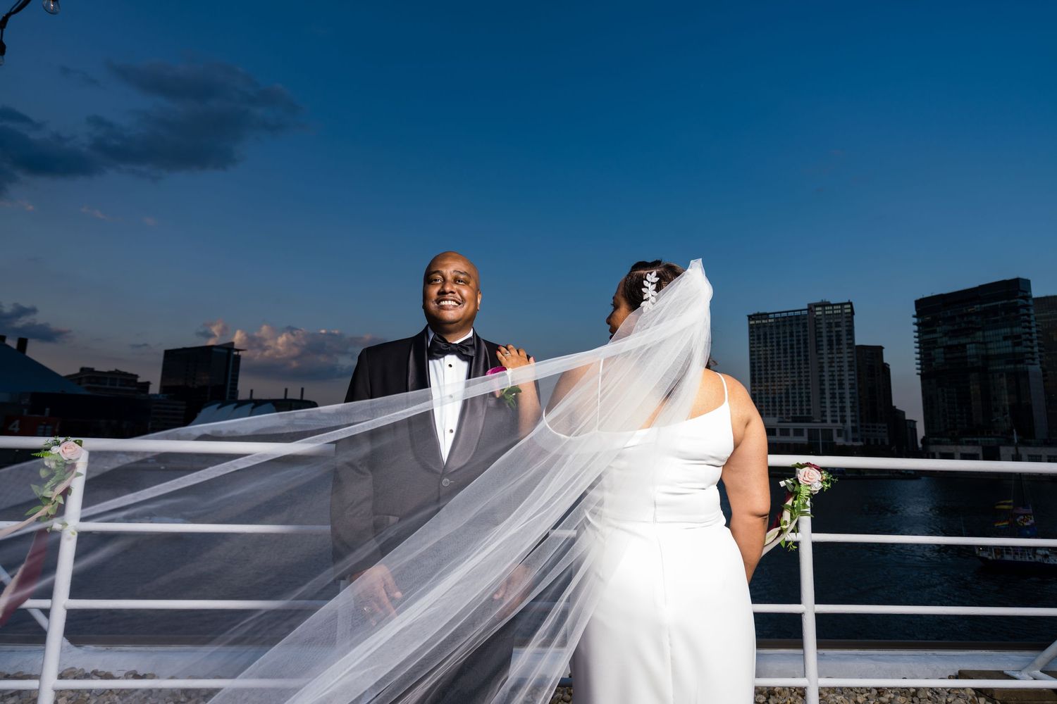 Wedding couple on rooftop with flowing veil against dramatic evening sky.