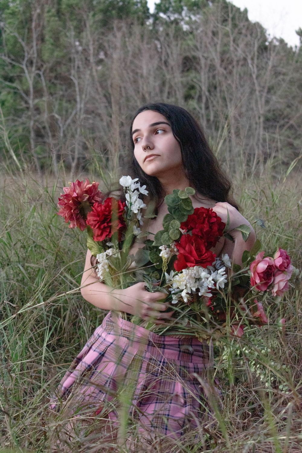 Romantic portrait with red flowers and plaid skirt in a natural woodland setting.