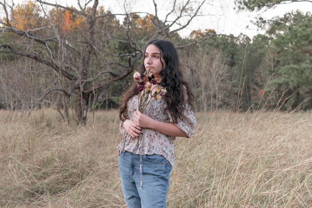 Candid outdoor portrait in jeans and floral top against a backdrop of autumn grass.
