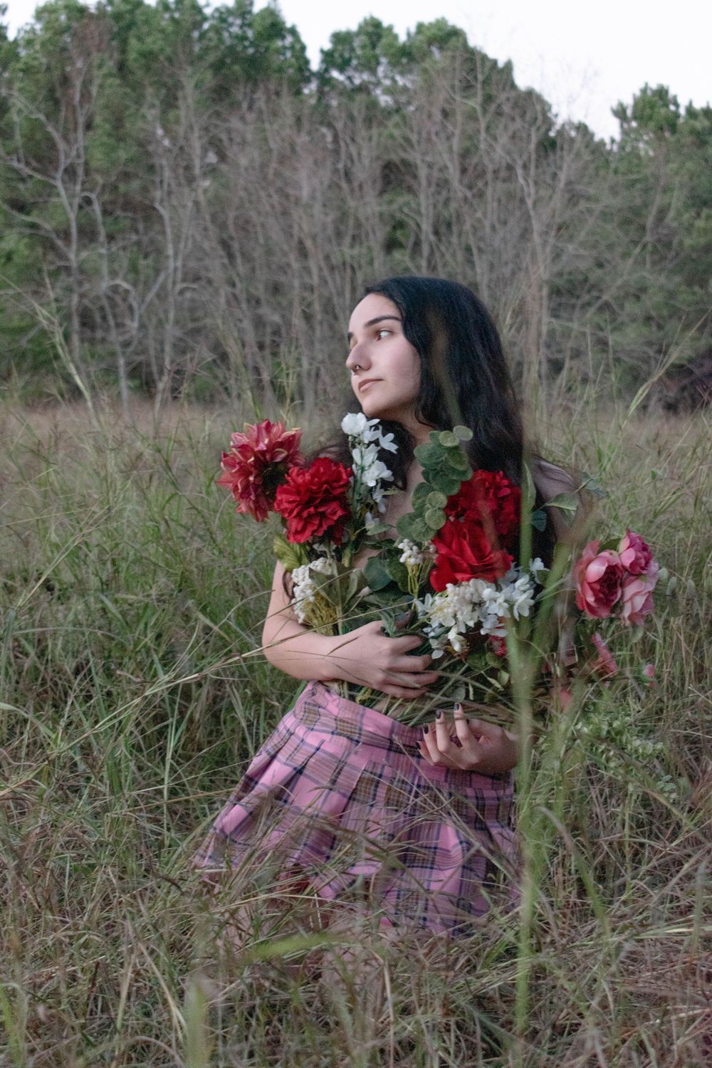 A dreamy outdoor portrait with vibrant red flowers and a pink plaid skirt in a rustic field setting.