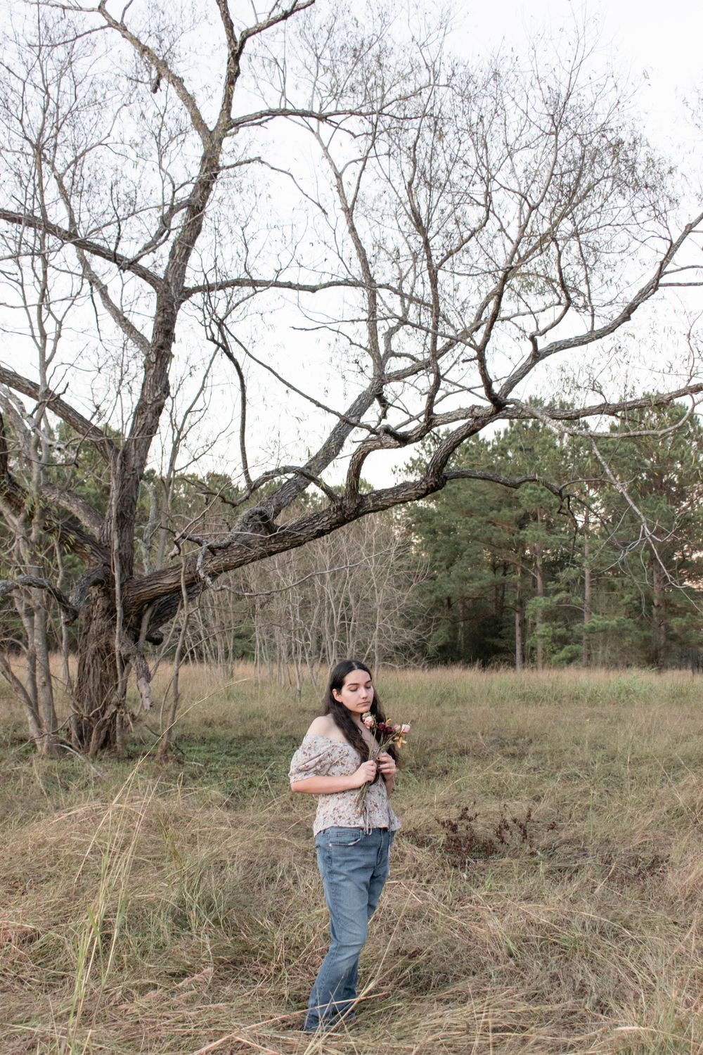 Artistic full-length portrait under bare branches in a field with natural winter lighting.