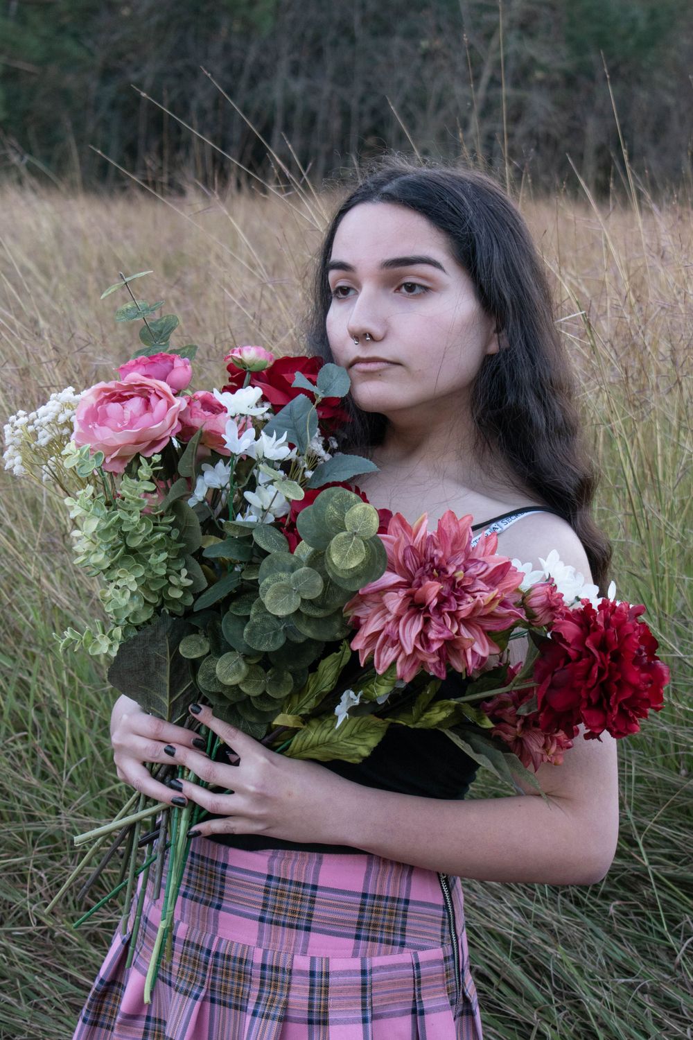 Vintage-inspired portrait with pink and red flowers against a rustic backdrop wearing a plaid skirt.