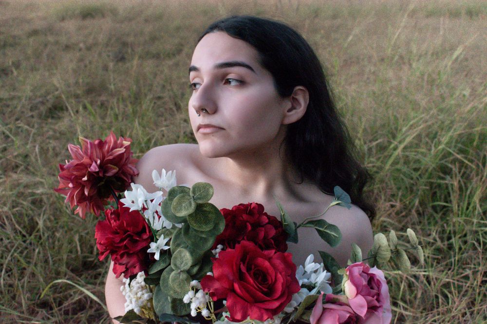 Artistic portrait with red and pink flowers against golden grass in soft lighting.
