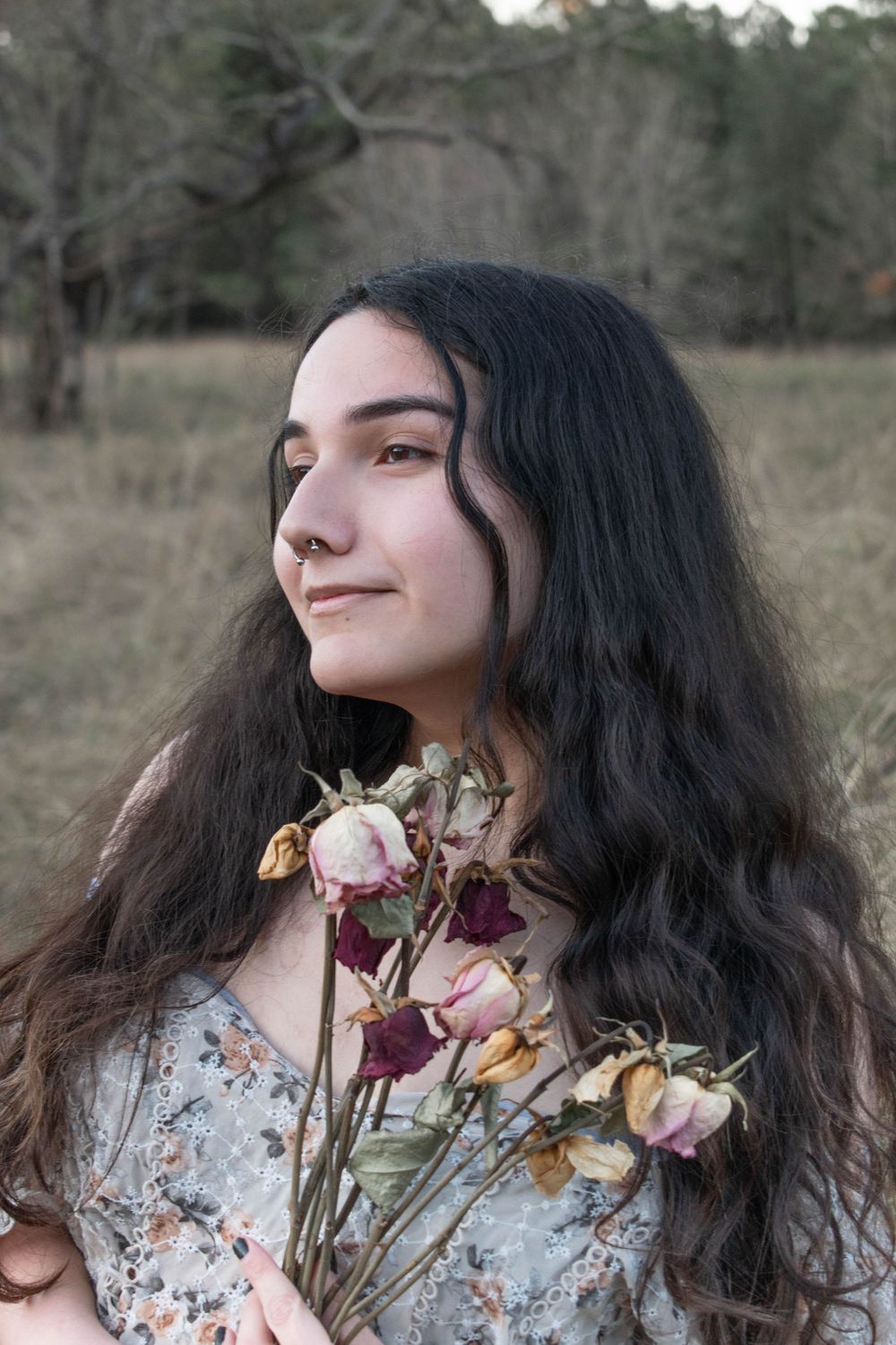 Long dark hair frames a portrait with dried flowers in a rustic outdoor setting.