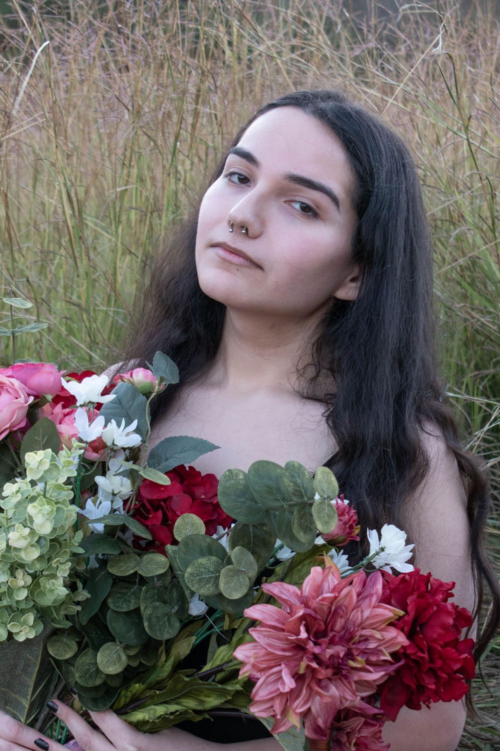 Ethereal portrait with a lush bouquet of pink and red flowers against tall grass in natural light.