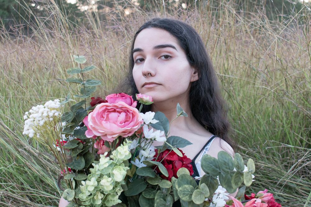Close-up portrait with a bouquet of pink roses and white flowers against tall grass and natural scenery.