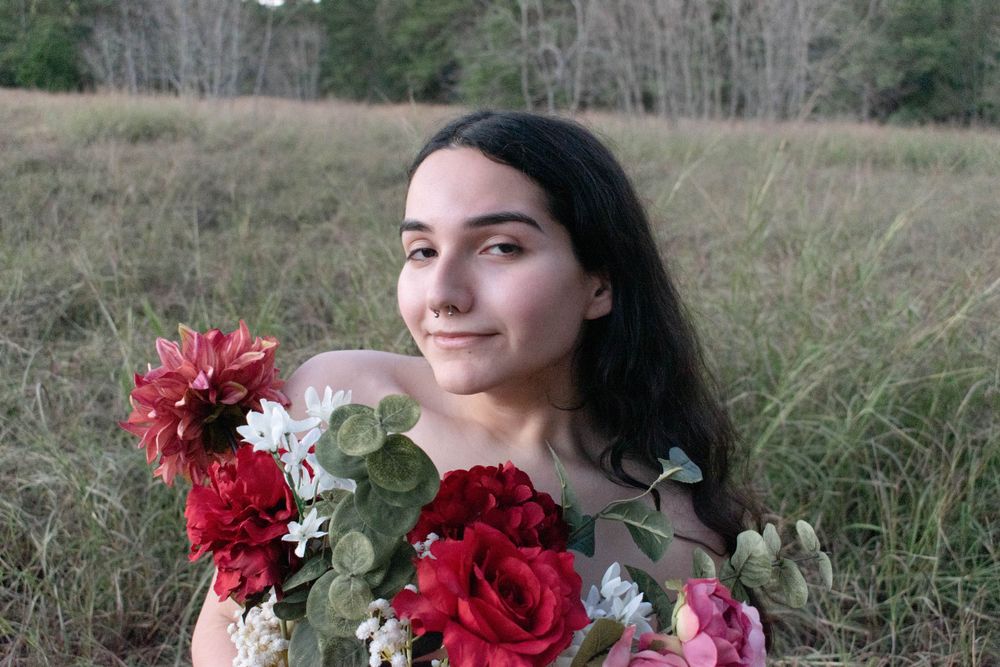 A bouquet of red roses and greenery frames an outdoor portrait in a natural field setting.