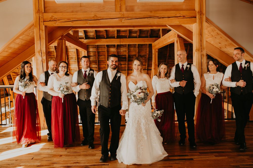 Bride and groom walk hand-in-hand through wedding party in a warm rustic barn setting.