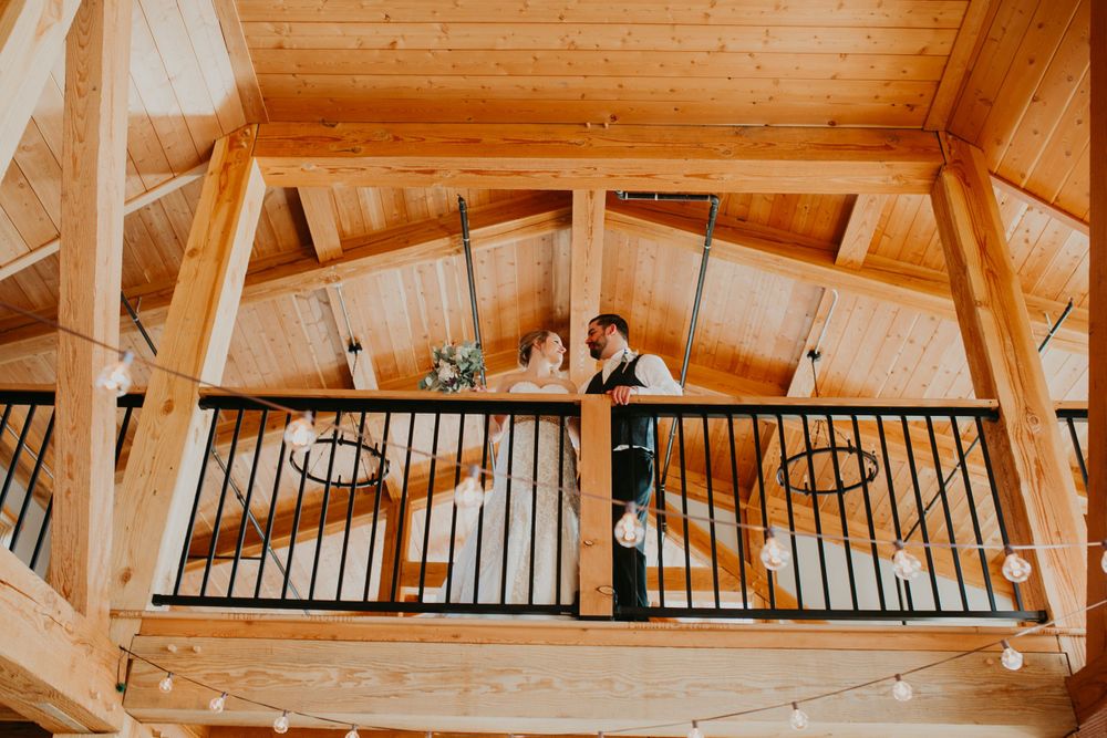 Bride and groom share a romantic moment on a wooden loft balcony inside a rustic barn wedding venue.