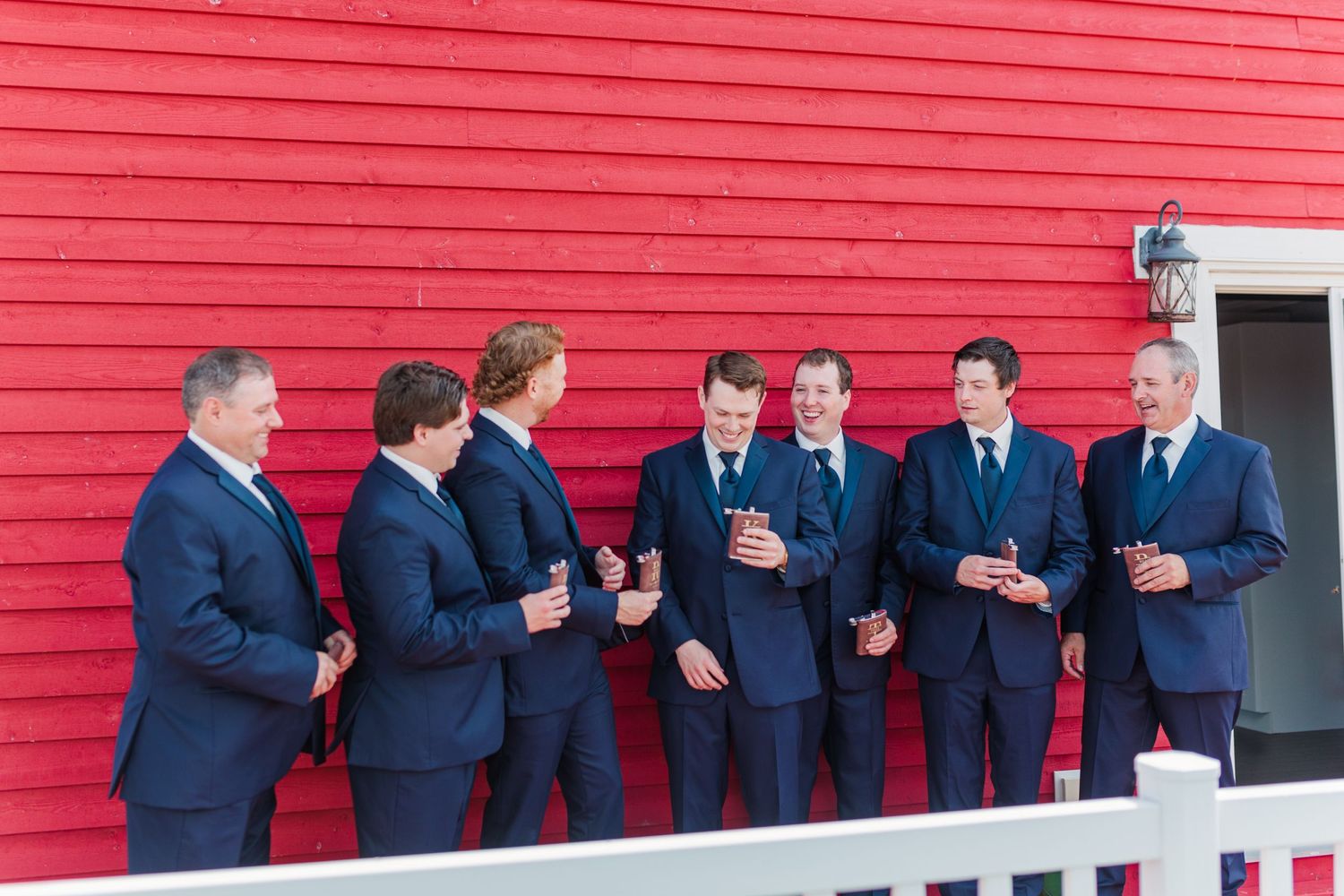 Line of groomsmen in navy suits posing playfully against bright red wall.