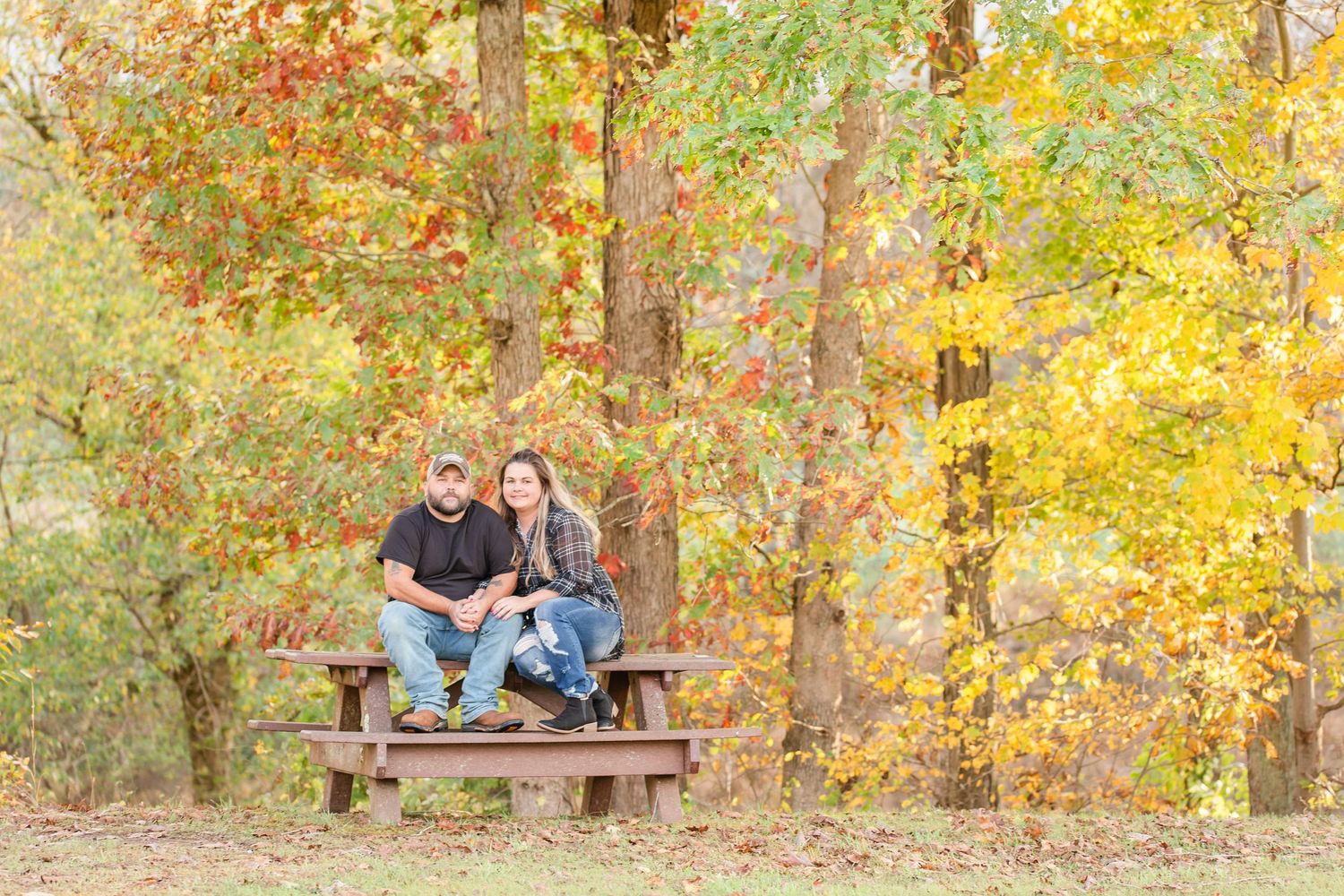 Autumn engagement photos show couple posing in park with vibrant fall colors in background.