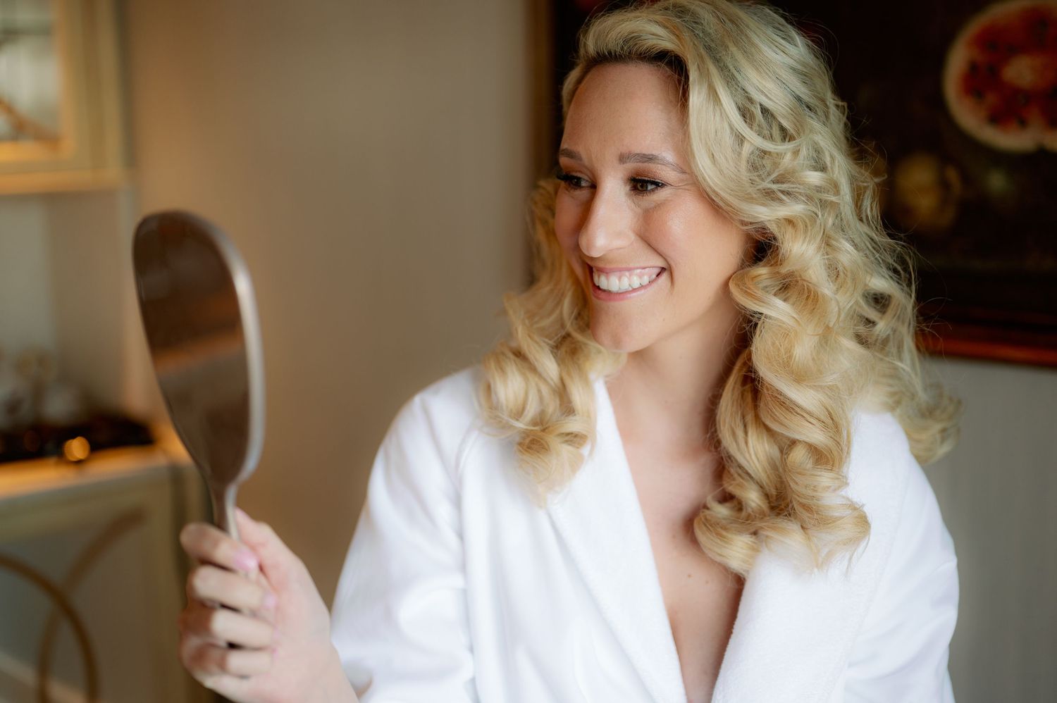 A person in a white robe holds a mirror while getting ready on their wedding day.