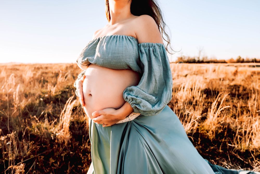 Maternity photos captured in warm golden light among natural grasses.