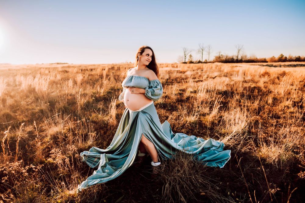 Artistic maternity portraits with flowing fabric in a sun-kissed field.
