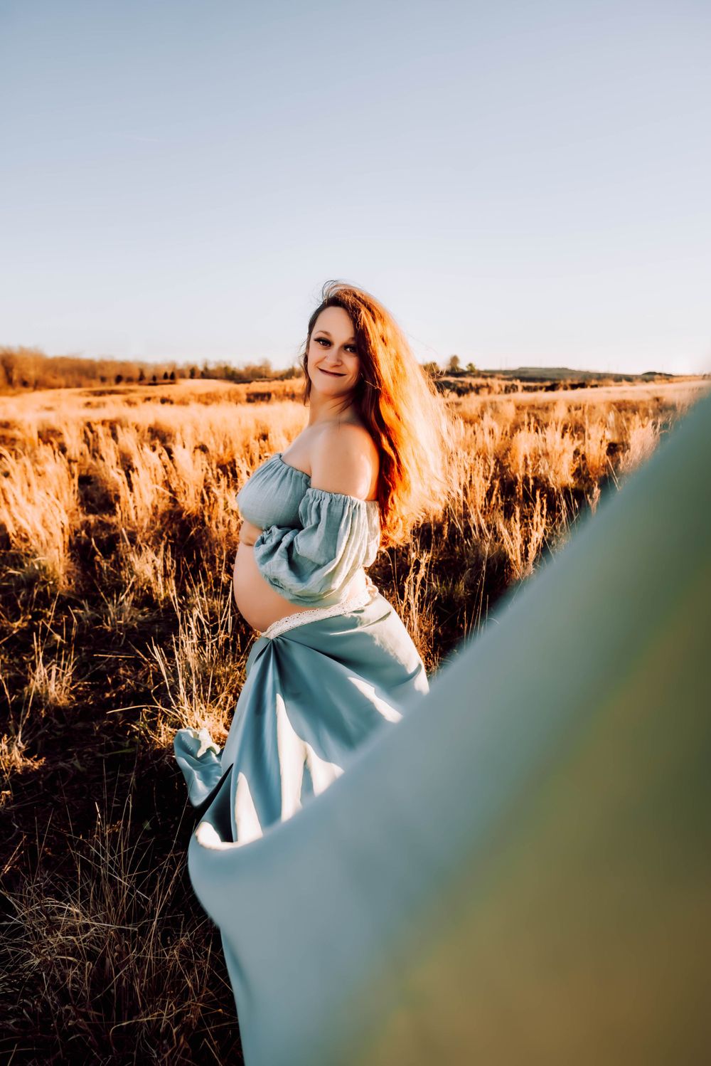 A flowing blue dress catches light in a golden field during sunset.