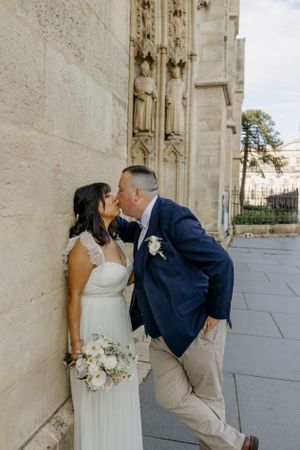 A couple shares their first kiss as newlyweds outside a gothic cathedral.