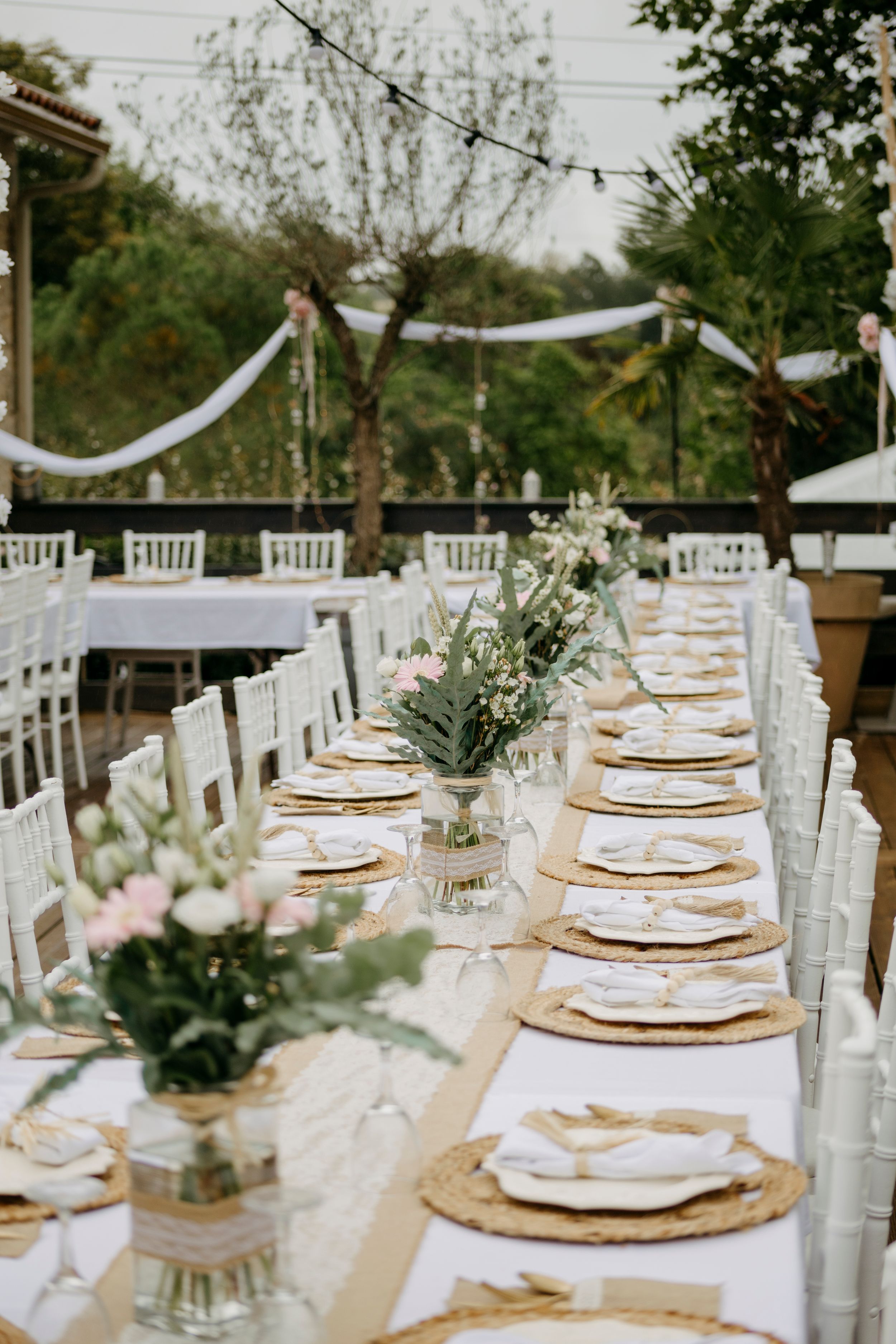 Elegant outdoor wedding reception table with white and gold place settings and floral centerpieces.