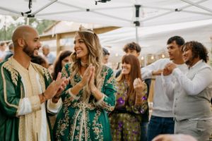 Wedding celebration scene with guests in formal attire gathered under white canopy decorations.
