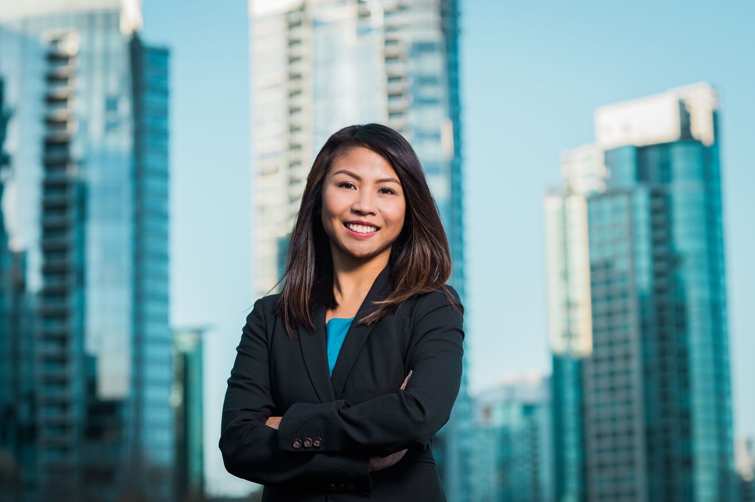 Professional stands confidently against modern city skyline of glass buildings.