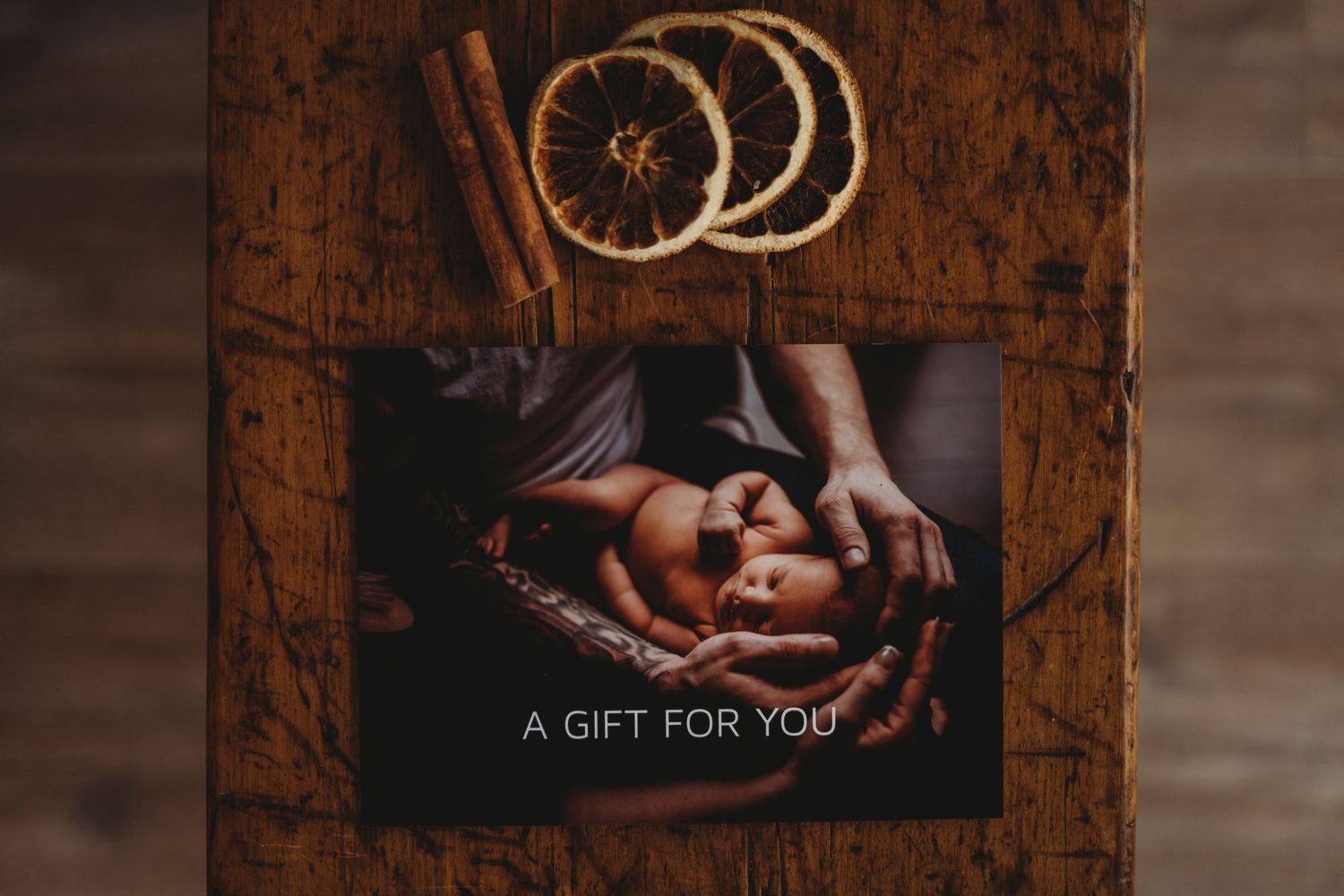 Gift card with cinnamon sticks and dried orange slices on rustic wooden background.