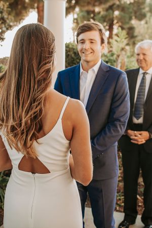 A wedding ceremony moment under white columns with garden greenery in the background.