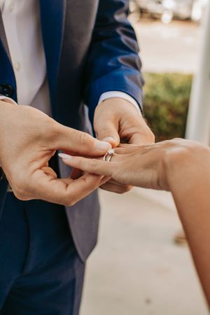 A close-up of hands during a wedding ring exchange ceremony outdoors.