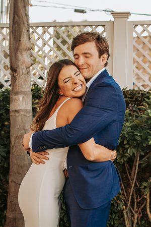 A joyful embrace between newlyweds under a white lattice pergola.