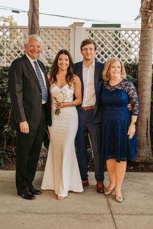 Family portrait at a wedding with formal attire standing against white lattice and greenery.