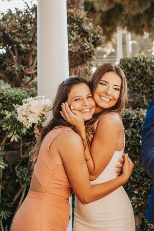 Two women in formal dresses share a joyful embrace at a wedding celebration.