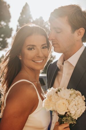 Sun-kissed wedding portrait with white roses and elegant attire.