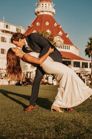 Romantic dip pose between newlyweds on the lawn with Hotel del Coronado's distinctive architecture behind them.