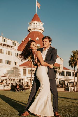 Dancing couple in wedding attire share a joyful moment in front of the Hotel del Coronado.