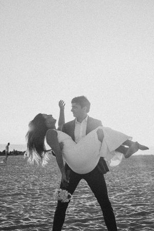 A romantic black and white beach photo of a couple embracing with a dip pose at sunset.