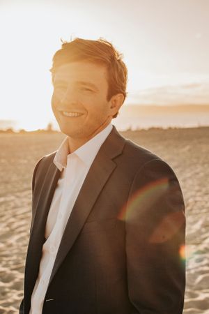 Golden hour portrait of someone in business attire smiling on a sandy beach.