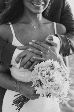Black and white close-up of hands holding a white floral wedding bouquet.