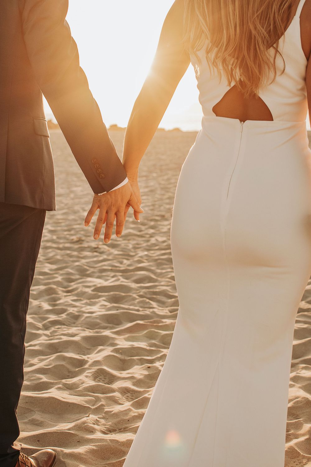Sunset silhouette of a couple holding hands on a sandy beach.