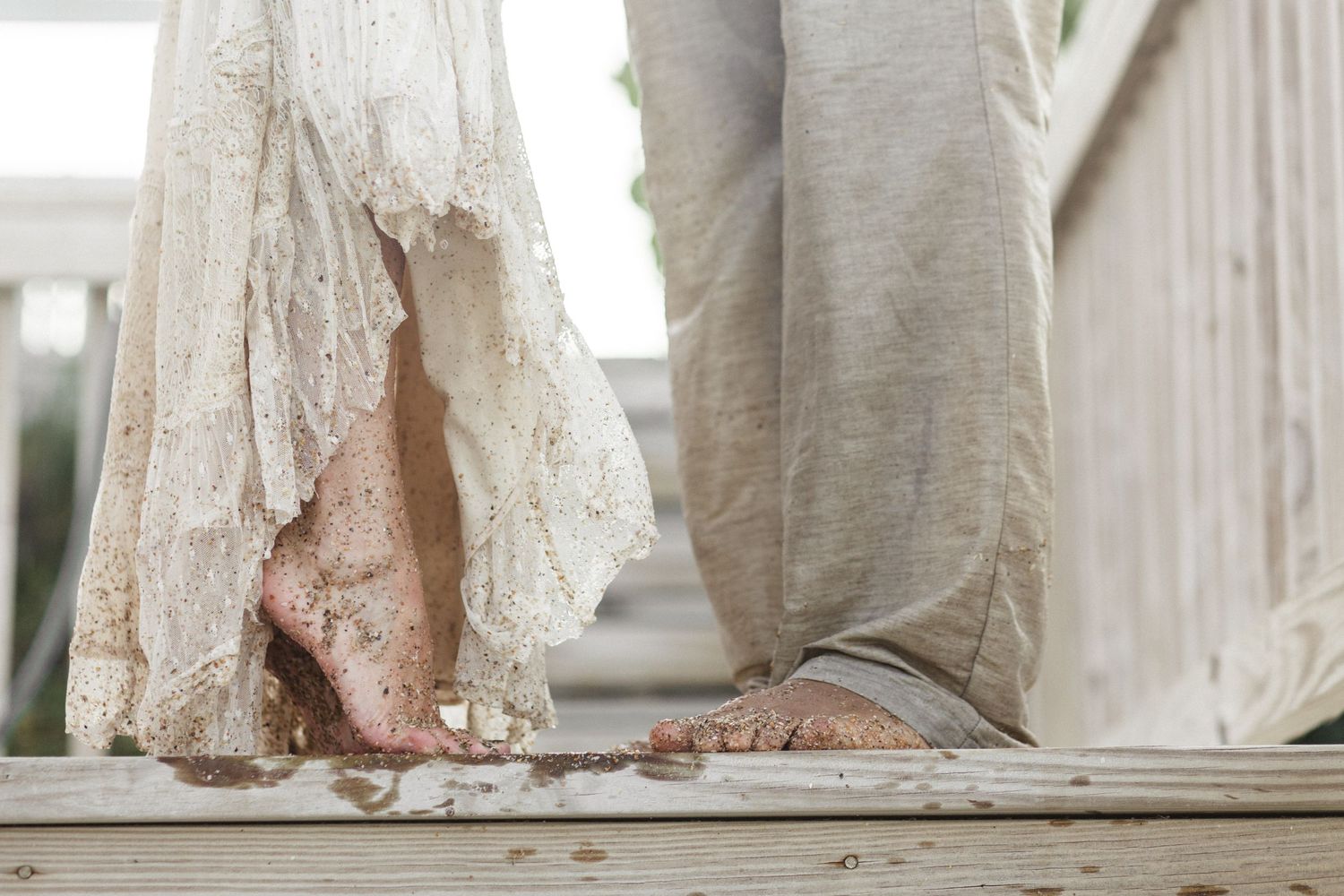 Close-up of bride and groom's feet on wooden deck, showing lace wedding dress detail.
