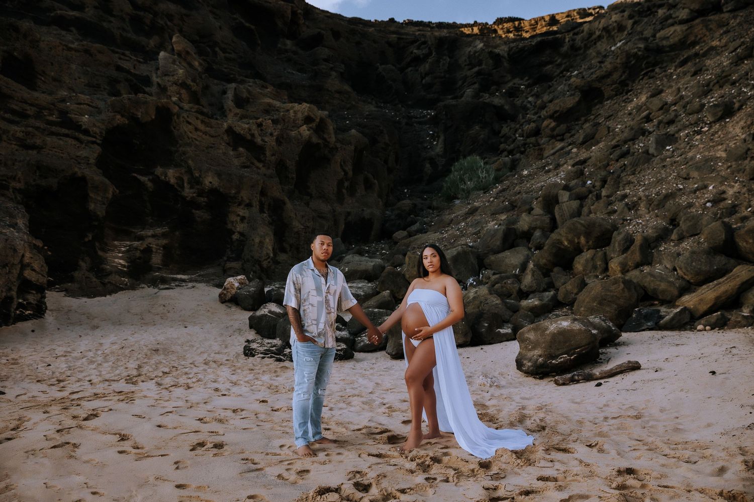 A couple poses together on a secluded beach surrounded by rocky cliffs.